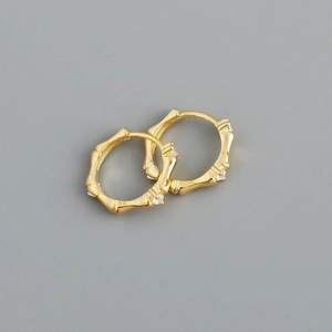 Detailed view of gold bamboo hoop earrings with small crystals on a grey background