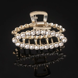 Close-up of golden hair claw clip with sparkling rhinestones and pearls on black background