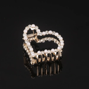 Macro view of a heart-shaped gold hair claw clip with inlaid pearls and sparkling crystals