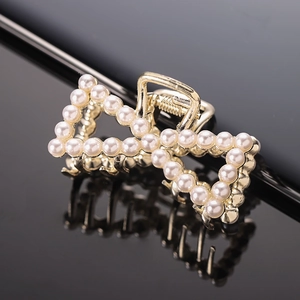 Close-up of golden bow hair claw clip with white faux pearls on black reflective surface