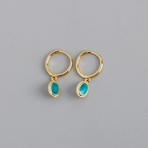 Close-up of golden hoop earrings featuring oval turquoise pendants with textured edges