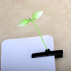 Detail shot of a creative green sprout hair clip on a white display card backing