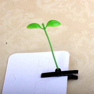 Detail view of the cute green sprout hair clip attached to white cardboard packaging.