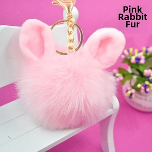 Close-up of fluffy pink rabbit fur pom pom keychain with gold ring on white bench