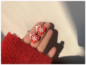 Close-up of red Christmas bell earrings with white snowflakes held in hand