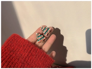 Detailed close-up of cute green Christmas tree resin earrings held against a red sweater