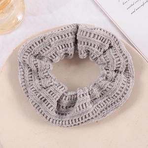 Close-up of a grey knitted velvet scrunchie on a beige tray with elegant aesthetic props