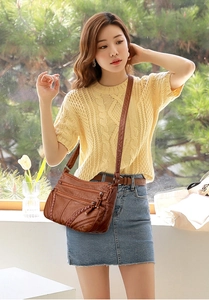 Brown soft leather crossbody bag with multiple zippers and woven strap detail on model