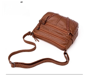 Detail view of brown faux leather crossbody bag with multiple zippers and woven texture
