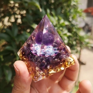 Detail of amethyst crystal pyramid with flower of life and gold foil held in hand