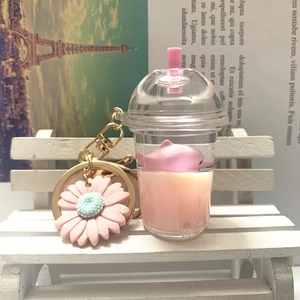 Detail of cute milk tea cup keychain with pink dolphin and daisy charm on a white bench