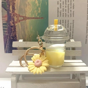 Detail of yellow milk tea cup keychain with daisy charm on a white mini wooden bench