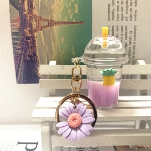 Detail of a purple daisy charm and mini milk tea cup keychain with liquid and pineapple