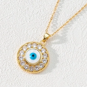 Macro detail of gold evil eye pendant featuring white zircon inlay and blue enamel center