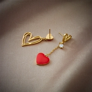 Asymmetric heart drop earrings with hollow gold design and red pendant on champagne satin