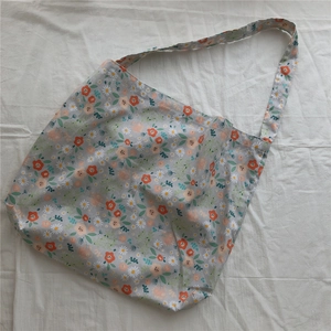 Flat lay of floral cotton shoulder bag with orange and white flowers on light gray fabric
