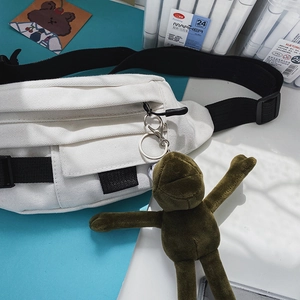 Detaillierte Draufsicht einer weißen Canvas-Brusttasche mit Gurt und grünem Froschanhänger