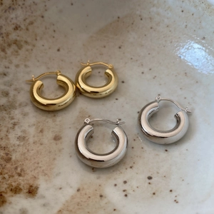 Close-up of thick gold and silver S925 sterling silver hoop earrings on ceramic plate