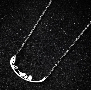 Silver stainless steel necklace with two birds on a branch pendant shown on dark background
