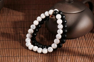 Detail of white turquoise and matte black beaded bracelets leaning on a ceramic teapot