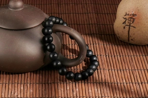 Zen style black beaded elastic bracelet wrapped around a teapot with bamboo backdrop