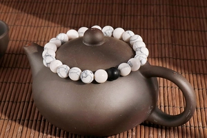 Detail of white turquoise beaded bracelet with one black bead on a vintage teapot lid