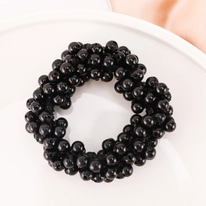Detailed close-up of a black pearl hair tie with smooth beads on white satin background