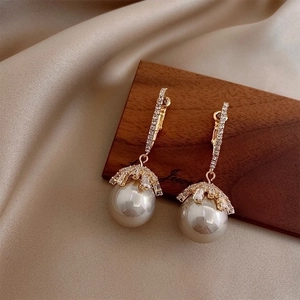 Elegant gold earrings with pearls and zircons displayed on silk fabric for women