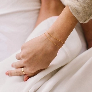 Detail of minimalist 14K gold double-layered beaded chain bracelet and round ring on wrist
