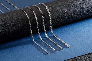 Close-up of four silver stainless steel chains in different thickness on a dark display
