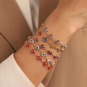 Close-up of stacked colorful Evil Eye bracelets with gold chains on a model's wrist