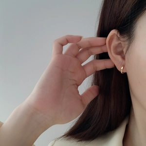 Close-up of a minimalist faceted gold huggie earring worn on a model's ear