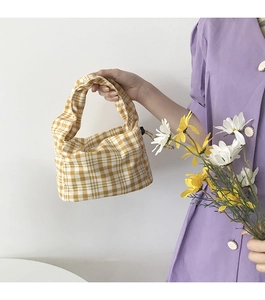 Détail d'un sac à main en toile à carreaux jaunes tenu avec un bouquet de marguerites
