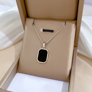 Detail of silver chain necklace with black rectangular pendant in a beige gift box