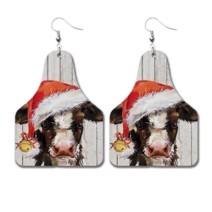 Detail view of festive cow-shaped earrings wearing a Santa hat with golden bell on white background