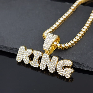 Close-up of gold KING letter pendant with sparkling rhinestones on a dark reflective surface