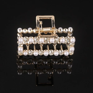 Close-up of golden hollow rectangle hair claw with white pearls and sparkling rhinestones