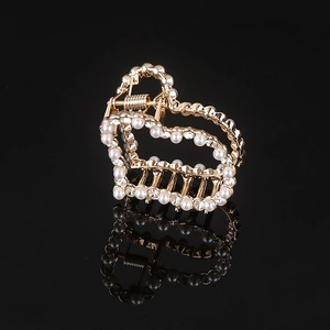 Macro detail of a golden heart hair claw clip with inlaid pearls and sparkling rhinestones
