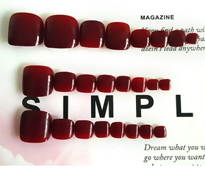 Flat lay of red glossy press-on toenails displayed on an open magazine background