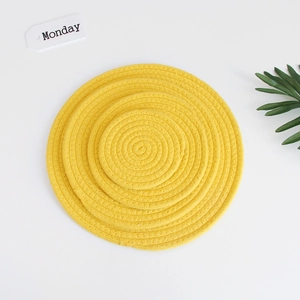Three sizes of yellow woven cotton rope coasters stacked on a white background with plant