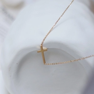 Close-up of minimalist gold cross necklace draped over a white ceramic dish