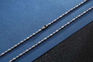 Macro detail of silver stainless steel ball chain necklace showing polished metal texture