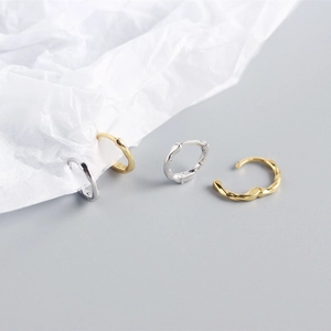 Artistic detail of gold and silver twisted hoop earrings on a minimalist paper background