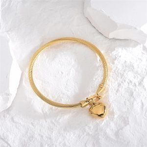 Gold twisted rope bangle with heart pendant on white stone background, minimalist style