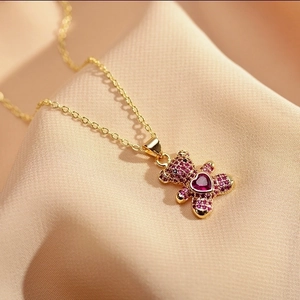 Macro view of gold teddy bear pendant with magenta crystals on soft beige fabric