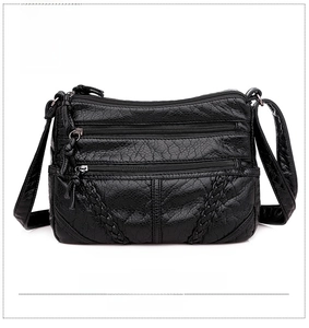 Detail of black faux leather crossbody bag featuring triple zipper pockets and woven trim