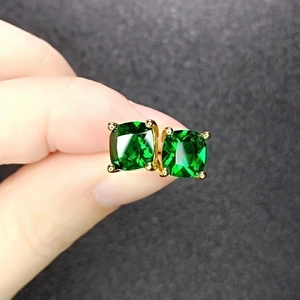 Green princess cut crystal stud earrings with gold four-prong setting held in hand