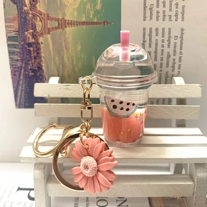Detail of pink milk tea acrylic keychain with golden daisy charm on a white mini bench
