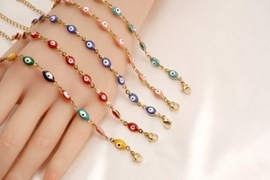 Detail of colorful Evil Eye charm bracelets stacked on a wrist with gold-tone metal chains