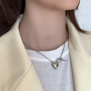 Detailed view of a silver heart necklace featuring a toggle clasp on a stylish model